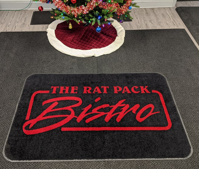 A close up image of the Rat Pack Bistro custom logo mat with a black background and red lettering