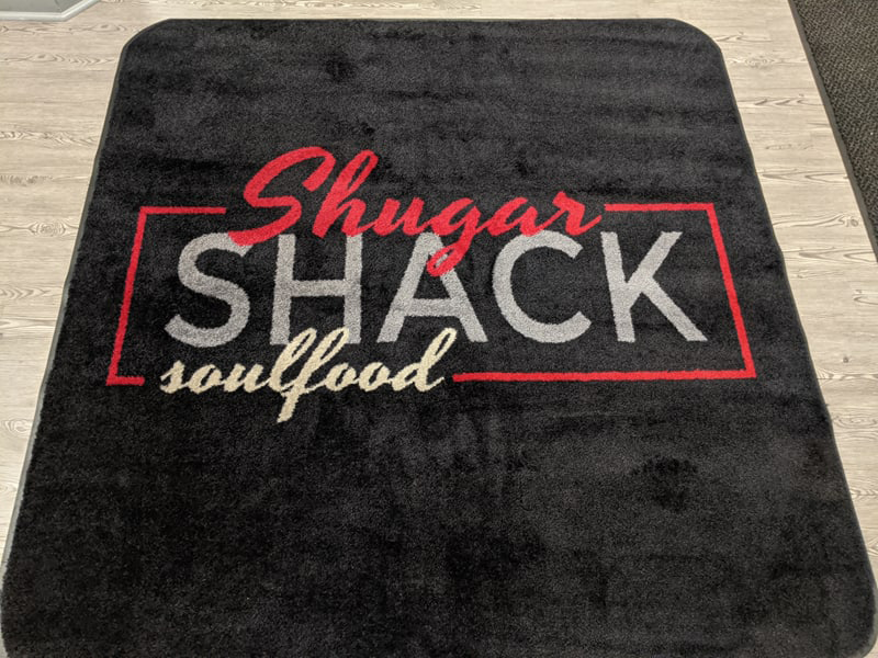 The Shugarshack Soulfood custom logo mat with a black background with red, white & grey lettering