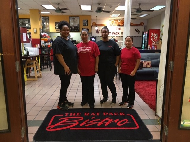 The four women of the Rat Pack Bistro team standing together behind their custom logo entrance mat