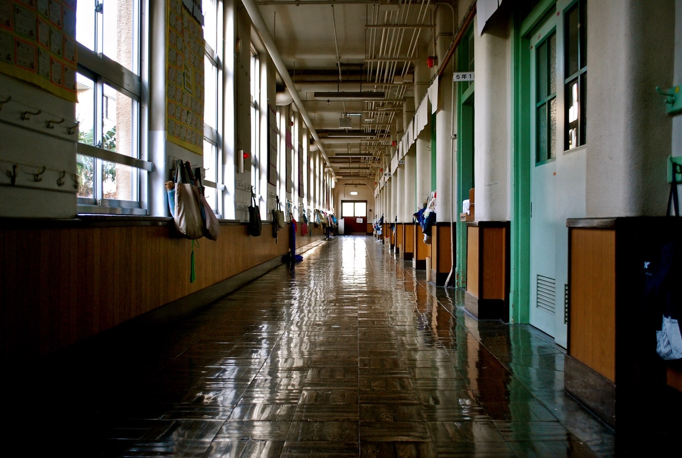 A quiet hallway in school during the day with backpacks hanging on the wall