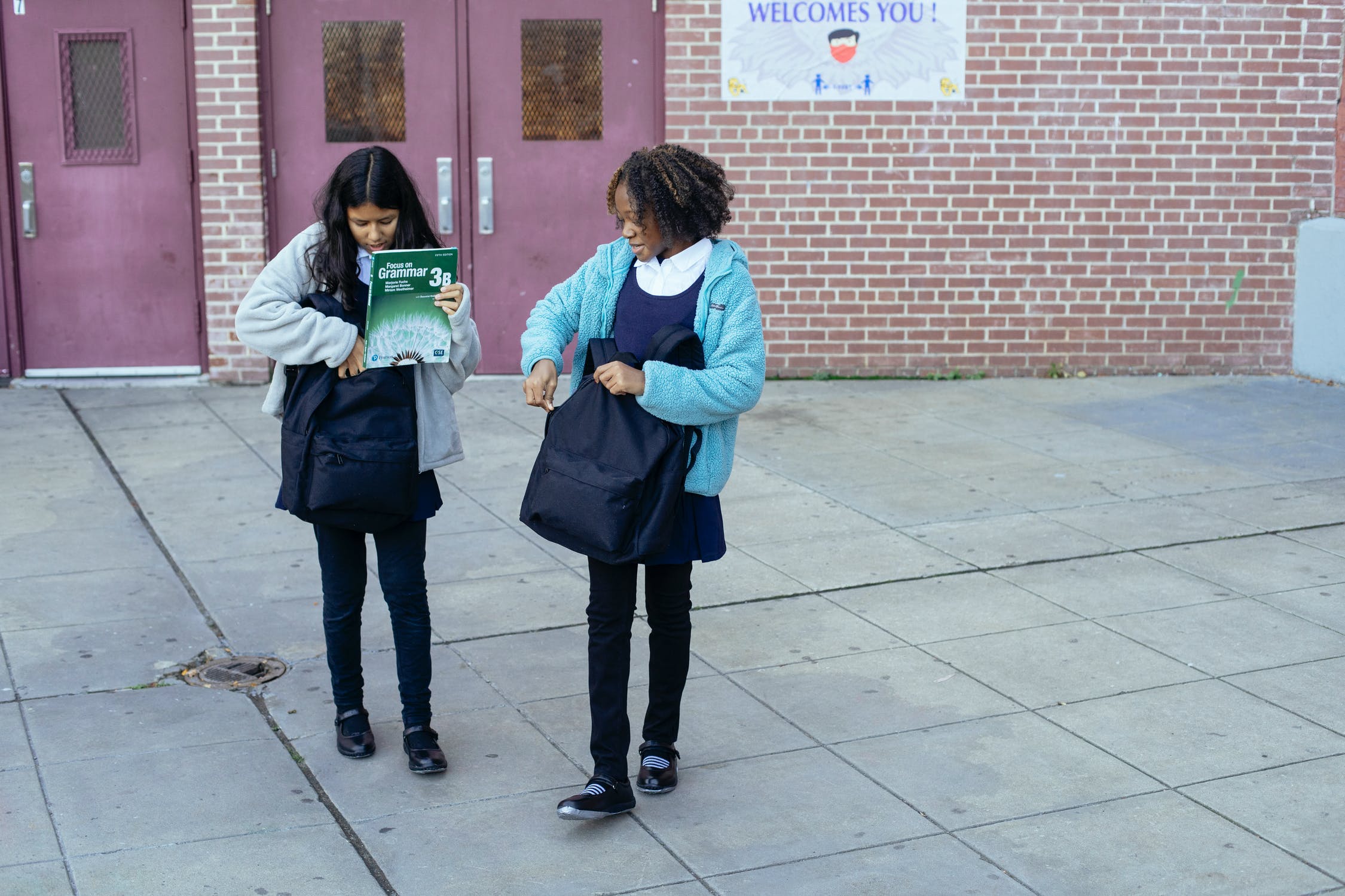 Two Girls in Uniform Leaving Elementary School at the End of the Day Putting Books in their Backpacks